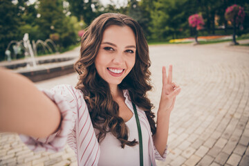 Poster - Photo portrait of female blogger with brunette curly hair taking selfie smiling showing v-sign gesture peace with two fingers