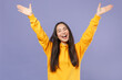 Joyful cheerful laughing attractive young brunette asian woman in casual basic yellow hoodie standing rising spreading hands looking camera isolated on pastel violet colour background studio portrait.