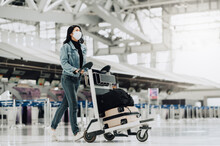 Happy Asian Tourist Woman With Mask Protection For Coronavirus Walking With Luggage Trolley Ready For Travel