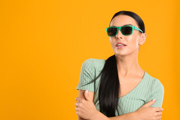 Wall Mural - Beautiful woman wearing sunglasses on yellow background. Space for text