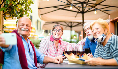 Senior couples taking selfie at restaurant bar with face masks - New normal lifestyle concept with happy people having fun together outdoors in covid-19 time - Focus on woman with glasses