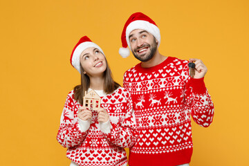 Wall Mural - Pensive young Santa couple friends man woman 20s in red sweater Christmas hat hold house bunch of apartment keys isolated on yellow background studio. Happy New Year celebration merry holiday concept.