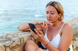 © Cavan Images - Attractive blonde woman using her smartphone on the coast during her summer vacation