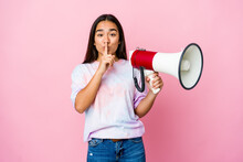 Young Asian Woman Holding A Megaphone Isolated On Pink Background Keeping A Secret Or Asking For Silence.
