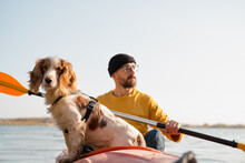 Man With A Dog In A Canoe On The Lake. Young Male Person With Spaniel In A Kayak Row Boat, Active Free Time With Pets, Companionship, Adventure Dogs