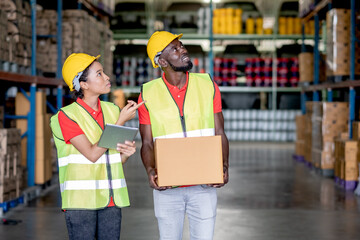 Wall Mural - African American warehouse man and woman or factory worker work and discuss together about product box that man holding and walk together in workplace. Concept of good management of staff working.