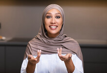 Muslim Woman Talking Looking At Camera Sitting In Kitchen Indoor