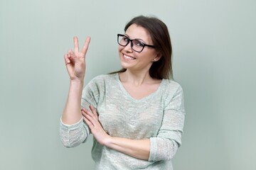 Happy mature confident woman showing victory symbol with hand gesture