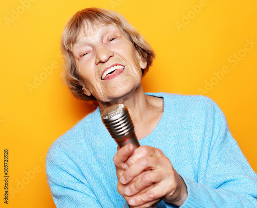 lifestyle and people concept: Happy old senior woman singing with microphone, having fun, expressing musical talent