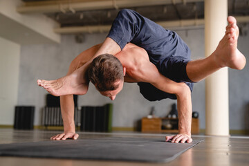 Wall Mural - Strong male yogi standing on his hands with both feet in the air indoors