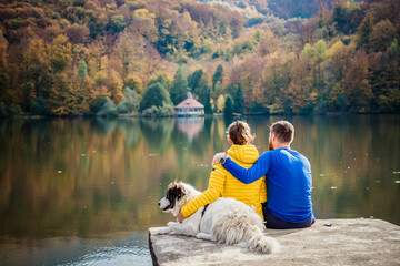 couple and dog sitting by beautiful autumn lake