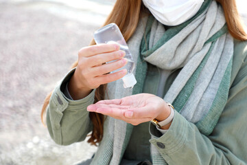 Wall Mural - COVID-19 Close up of woman hands sanitizing with alcohol gel from dispenser in city street. Focus on the hand.