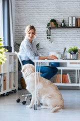 Sticker - Attractive young woman looking at her beautiful dog while working with laptop in living room at home.