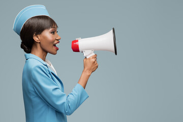 Wall Mural - Cheerful young african stewardess shouts into the loudspeaker. Blue background.