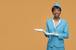 Smiling young african stewardess shows a welcome gesture. Orange background.