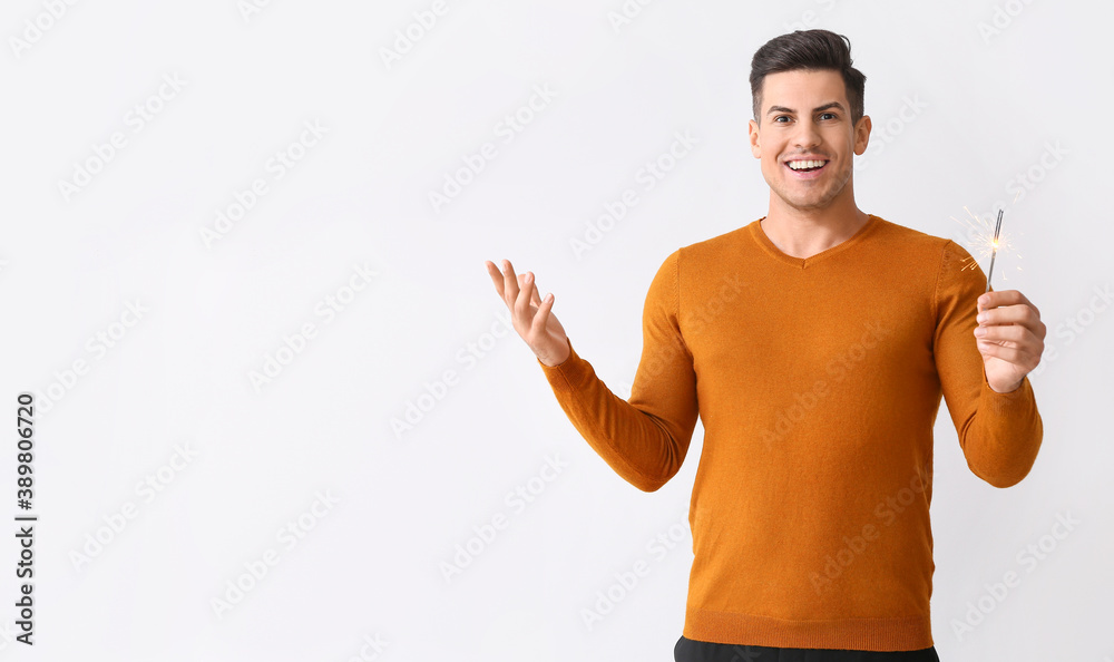 Handsome young man with Christmas sparklers on light background