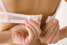 Young Adult Woman Hands Putting On Or Taking Off Bra. Daily Underwear. Closeup. Back View.