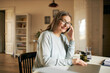 © shurkin_son - Horizontal image of beautiful retired woman copywriter working from home sitting at desk with portable computer, holding mobile, having nice phone conversation. Age, people and freelance concept