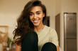 © shurkin_son - Indoor shot of beautiful happy young 20 year old Arabic woman relaxing at home wearing comfy clothing, looking at camera with broad smile, showing white straight teeth. Cute girl having rest indoors