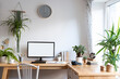 © photosbysabkapl - Modern interior of workplace at home with office desk and chair with blank white wall and window. Blank screen of computer with mock up, plant, clock and coffee. Mock up.