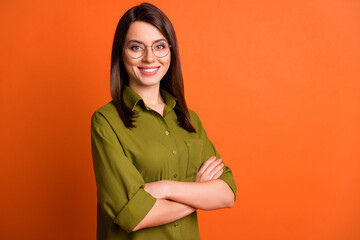 Photo portrait of cheerful girl with folded hands wearing glasses smiling isolated on vibrant orange color background with blank space