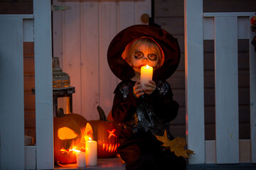 Scary toddler child in halloween costume, playing with carved pumpkins