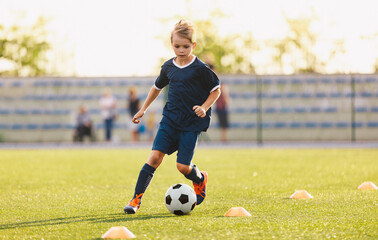 Young boy in blue soccer jersey uniform running after ball on training pitch. Kid improving dribbling skills on practice session