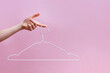 Feminine hand holding empty hanger isolated on pink background