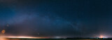 Fototapeta Niebo - Night Starry Sky With Glowing Stars Above Countryside Landscape. Milky Way Galaxy And Rural Field Meadow In Early Spring. Panorama, Panoramic View