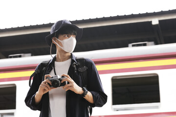 Wall Mural - Asian travelers men and camera in train station with medical face mask to protection the Covid-19, new normal lifestyle