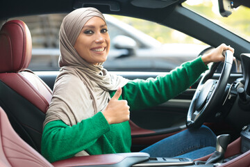 Wall Mural - Smiling muslim woman driving car, showing thumbs up