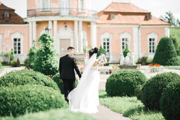 Stylish couple of happy newlyweds walking in the park on their wedding day with bouquet