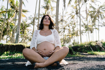 Poster - Positive pregnant woman sitting on wet ground in tropical forest