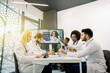 © sofiko14 - Team of multiracial five doctors sitting in light office, having video conference meeting with young, pretty African doctor, consulting her colleagues about the patient CT and treatment