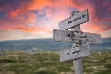 unlimited boundless infinite text engraved in wooden signpost outdoors in nature during sunset and p