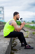 © Georgii - Athletic guy in stylish sportswear drinks water sitting on stairs after workout in cloudy weather outside