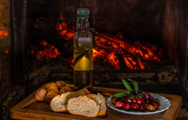 Olive oil flavoured with rosemary on a wooden tray accompanied by raw olives, bread and walnuts with a Chinese base and rustic fire