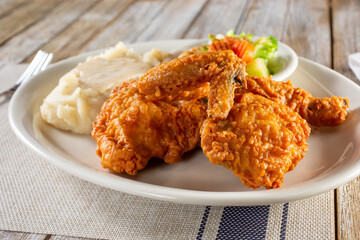 A view of a plate of fried chicken and mashed potatoes, in a restaurant or kitchen setting.