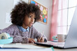 © insta_photos - Cute smart african american school pupil kid girl virtual distance learning online watching remote digital class lesson looking at laptop computer tech studying at home writing notes sitting at desk.