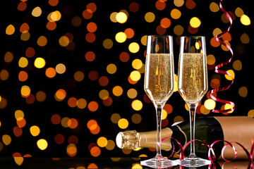 Bottle and glasses of champagne with ribbons on blurred lights background