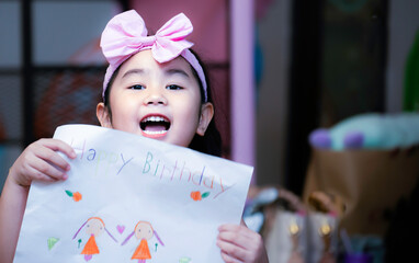 Happy birthday. Cheerful pretty birthday girl receiving a drawing from her close friend at her birthday party. Happy kid at a birthday party holding wonderful drawing receiving form friend.