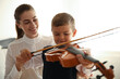 © New Africa - Young woman teaching little boy to play violin indoors