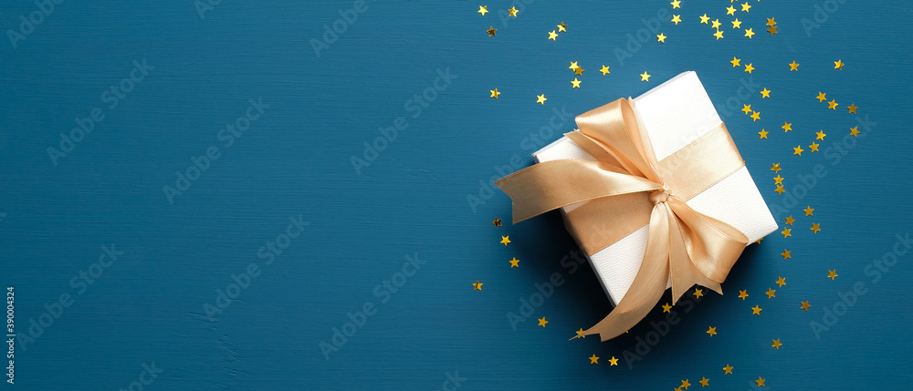 White gift box with golden ribbon bow on blue background with confetti ...