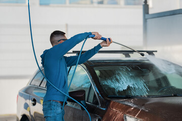 Wall Mural - Man washing car in self serve car wash. Cleaning car using high pressure water.