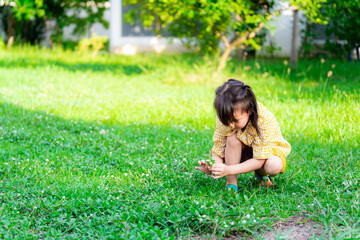 Girl in yellow dress was picking up the grass flower. Children squatting on the green lawn in an evening of summer or spring. Beautiful 5 year old child learns to play alone with nature.