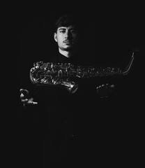 Wall Mural - Grayscale shot of a handsome guy tossing into the air his saxophone isolated on a dark background