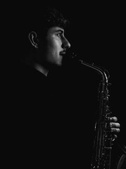 Wall Mural - Grayscale shot of a cool and handsome guy playing his saxophone isolated on a dark background