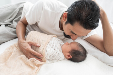 Canvas Print - father with a baby girl at home sleeping. side view of a young man playing with his little baby in bed. a portrait of a young Asian father holding his adorable baby on white background.