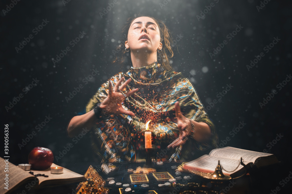 Astrology, magic and divination. The sorceress creates the magic of divination over a candle. Black background. There are magic items on the table - obrazy, fototapety, plakaty 