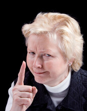 Studio Photo Of Older Woman With An Angry Look Making A Warning Finger Gesture. Black Background.